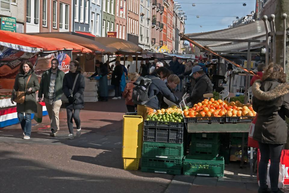 Puesto de un mercado callejero con cajas de fruta y clientes al fondo